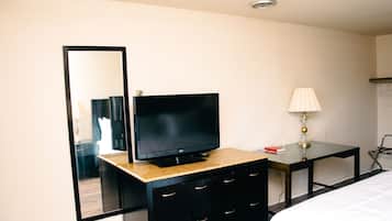Una habitación de hotel con televisor en una cómoda, un espejo, una lámpara y una cama.