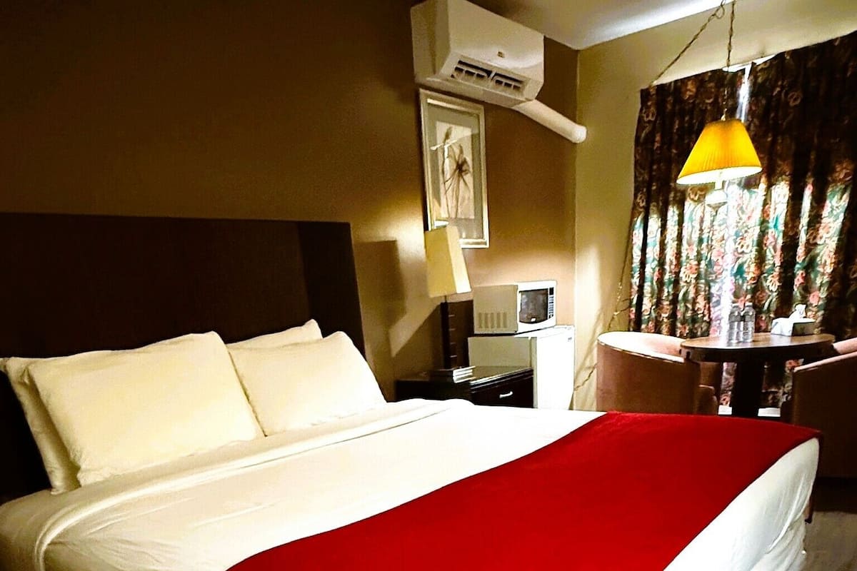 Een hotelkamer met een bed, een bureau, een stoel, een airconditioning en een lamp.