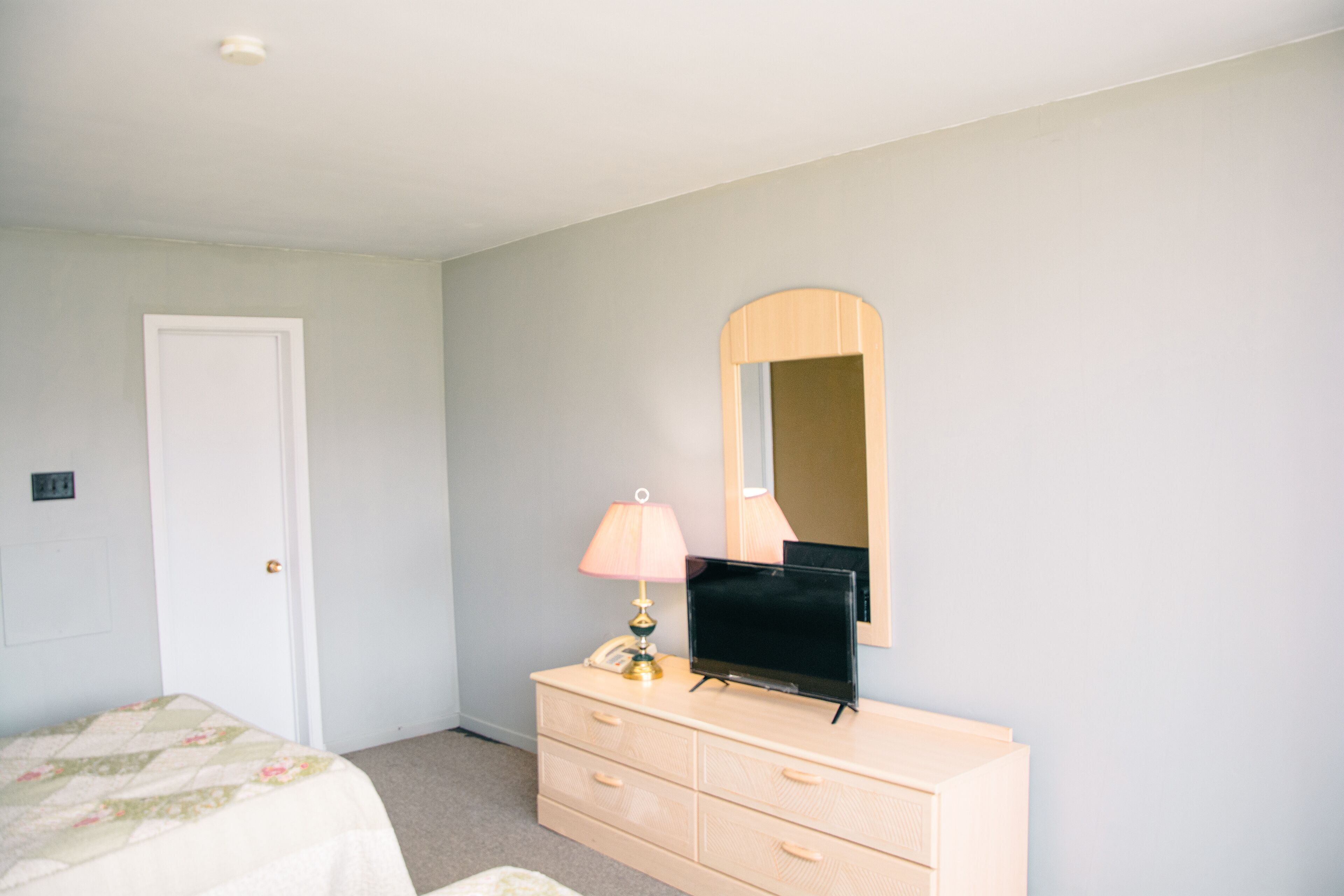 A bedroom with a bed, dresser, mirror, and lamp.