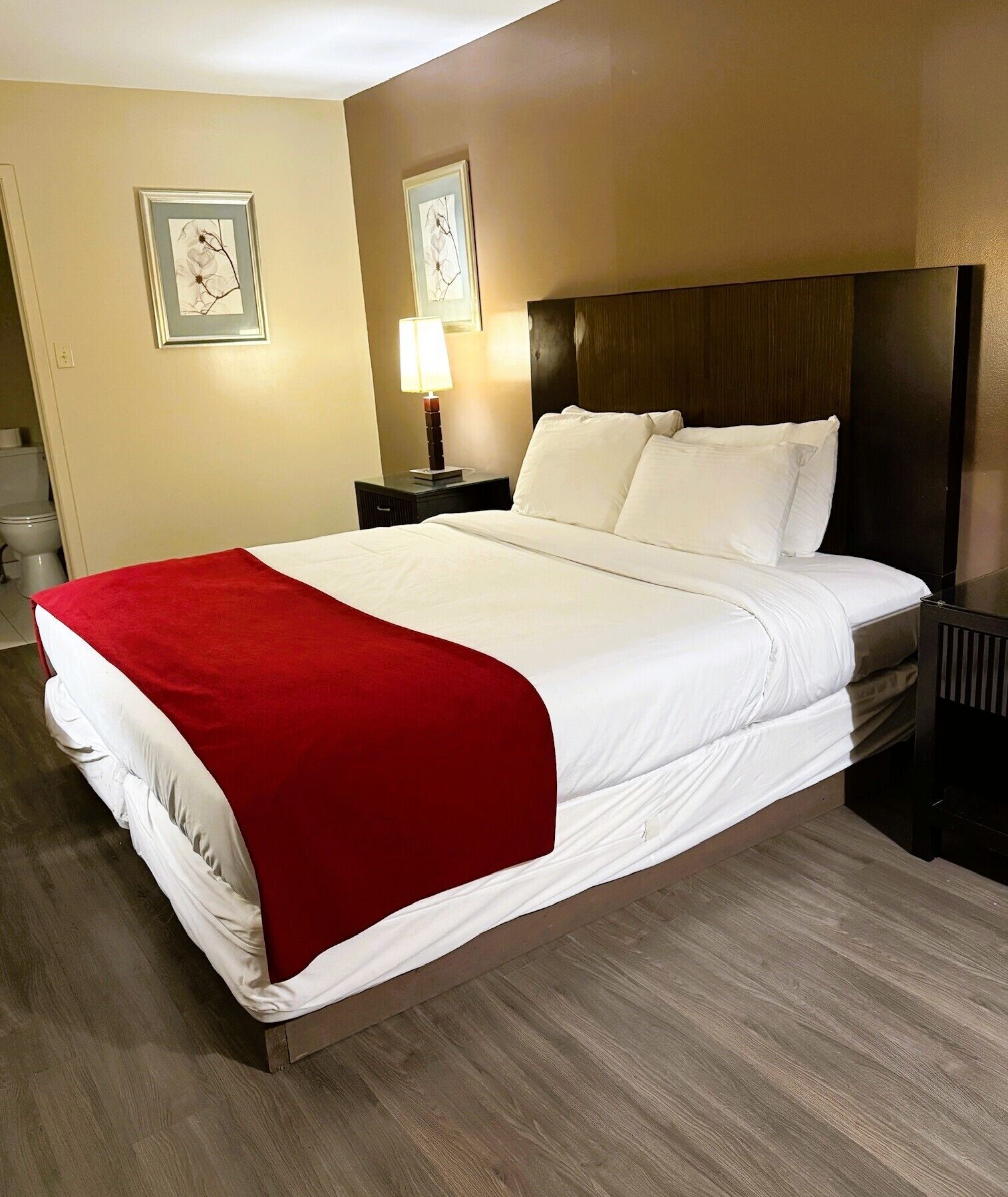 A hotel room with a large bed, a nightstand with a lamp, and two framed pictures on the wall.