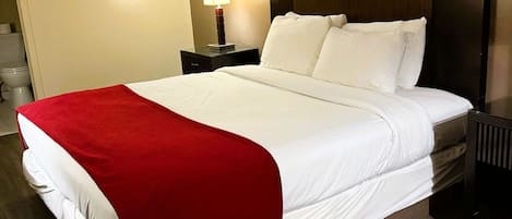 A hotel room with a large bed, a nightstand with a lamp, and two framed pictures on the wall.