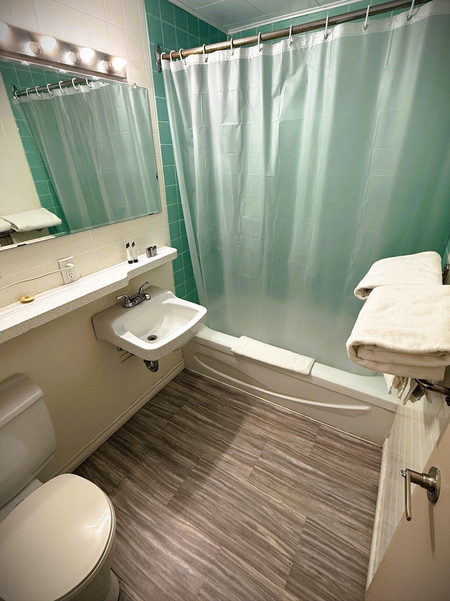 A bathroom with a shower curtain, sink, mirror, and a towel rack.