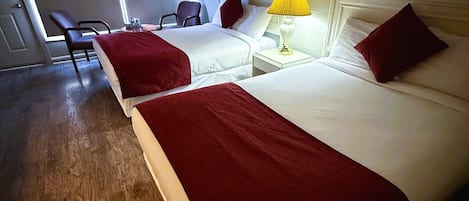 A hotel room with two beds, a chair, a table with a lamp, and a picture on the wall.