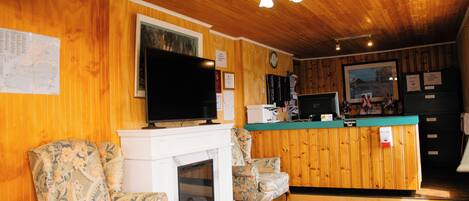 Un interior de madera con chimenea, dos sillones estampados, un televisor y un mostrador de recepción.