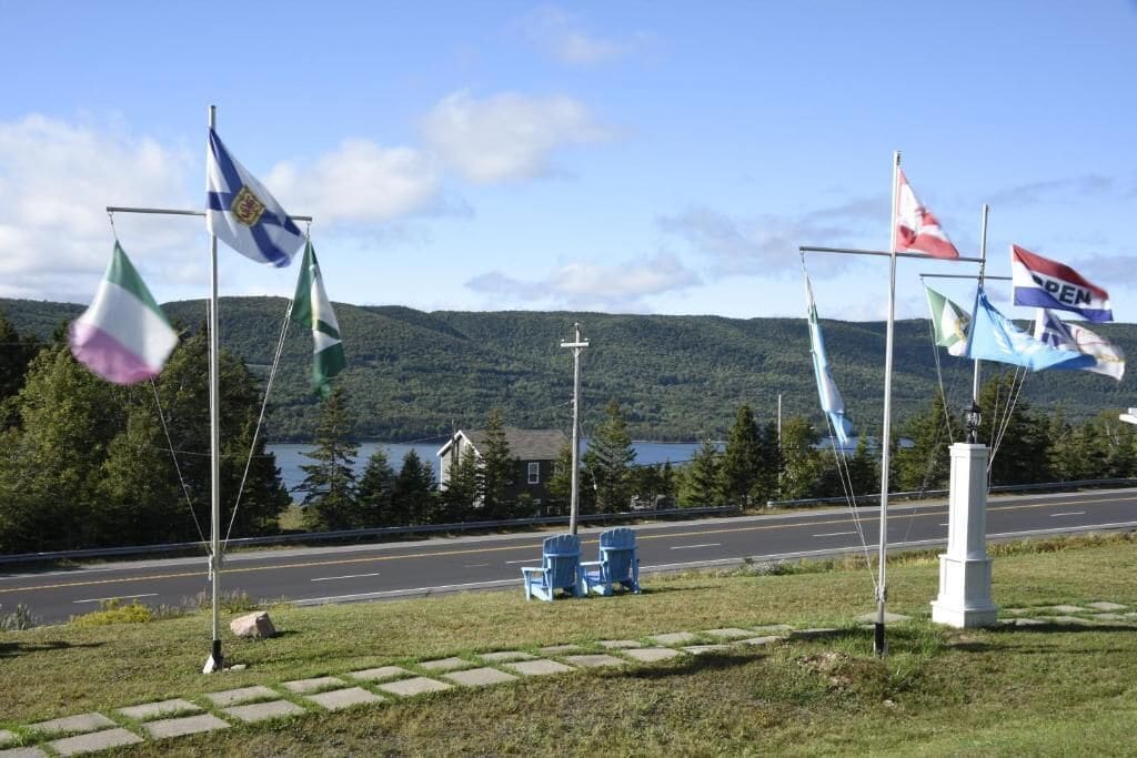 A road with flags on flagpoles, a grassy area, and a lake in the background.