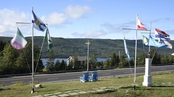 A road with flags on flagpoles, a grassy area, and a lake in the background.