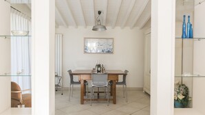 A dining area with a wooden table, metal chairs, a hanging light fixture, and a framed artwork on the wall. - Beautiful house with swimming pool surrounded by greenery, modern, luxury finishes (Camaiore)