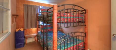 A bunk bed room with a wooden headboard, a window with curtains, and a small stool.
