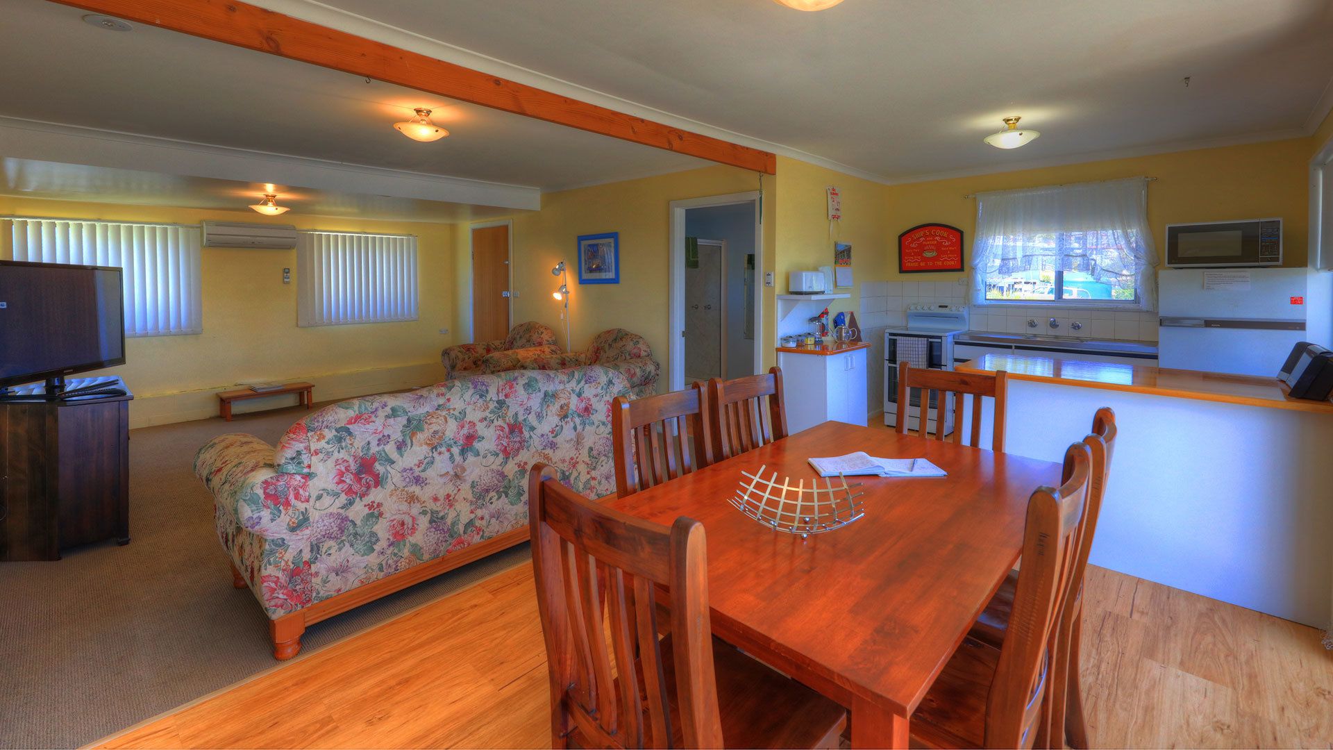 Una sala de estar acogedora con un sofá floral, una mesa de comedor de madera y una zona de cocina con microondas y estufa.