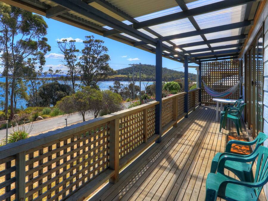 Une terrasse en bois avec vue sur la mer, un hamac et des chaises vertes.