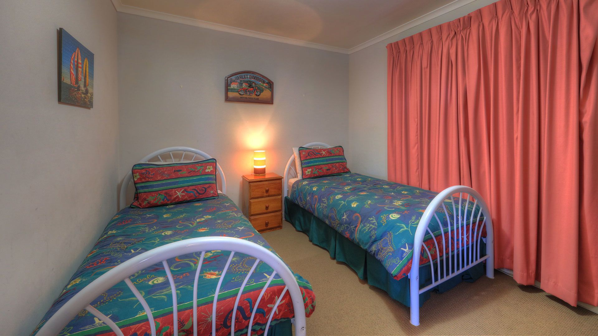 A bedroom with two single beds, a nightstand, a lamp, a wall clock, and a window with curtains.