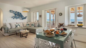A modern living room with a sofa, dining table, and chairs, a kitchen area with a view, and a decorative fish wall art piece. - H2O Private Villa Paros, infinity swimming pool, sea view lounge area, bbq & Bar (Koukoulavmes)