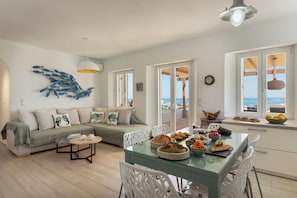 A modern living room with a sofa, dining table, and chairs, a kitchen area with a view, and a decorative fish wall art piece. - H2O Private Villa Paros, infinity swimming pool, sea view lounge area, bbq & Bar (Koukoulavmes)