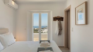 A bedroom with a bed, a view through a door, and a towel rack. - H2O Private Villa Paros, infinity swimming pool, sea view lounge area, bbq & Bar (Koukoulavmes)