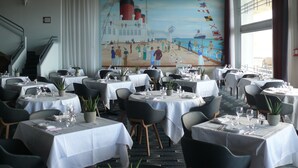 Un restaurante con mesas dispuestas para comer, un mural en la pared y una escalera que conduce a un nivel superior.