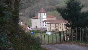 Un edificio histórico con una torre destacada, rodeado de vegetación y una zona delimitada por una cerca.