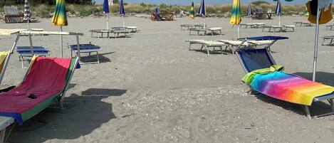 Une plage bordée de rangées de transats et de parasols, dont certains sont recouverts de tissus aux couleurs vives.