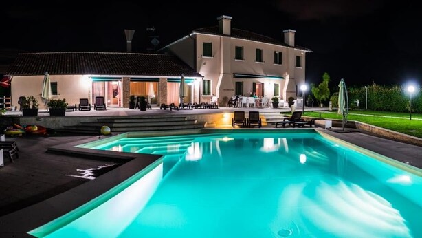 A nighttime view of a hotel with a swimming pool, outdoor seating, and a well-lit patio area.