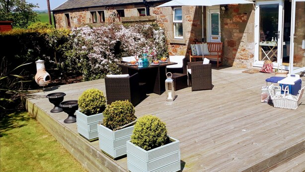 Een terras met buitenmeubilair, een tafel en plantenbakken.