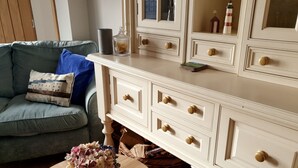 Een woonkamer met een grijze bank, een witte dressoir met meerdere lades, een vaas met bloemen en een kleine tafel met een kaart.