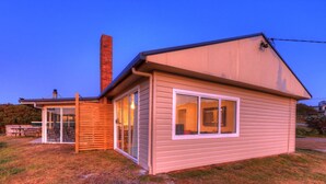 A single-story house with a chimney, a covered patio, and a large window. - Arthur River Spa Cottage (Arthur River)