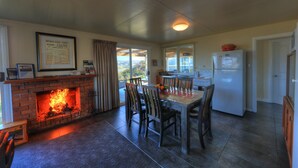 A kitchen with a fireplace, dining table, chairs, and a refrigerator. - Arthur River Spa Cottage (Arthur River)
