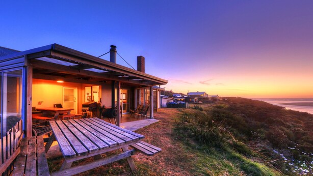 A modern house with a patio, large windows, and a view of the ocean at sunset. - Arthur River Spa Cottage (Arthur River)
