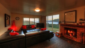 A living room with a black leather sofa, red cushions, a TV, and a fireplace. - Arthur River Spa Cottage (Arthur River)