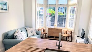 Una cocina con encimera de madera, un lavamanos, una mesa de comedor con sillas, un sofá con cojines estampados y una ventana con persianas.