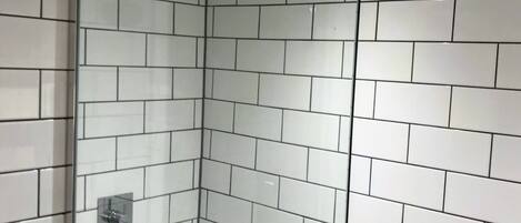Une douche fermée par des parois en verre, avec des carreaux blancs et une pomme de douche visible.