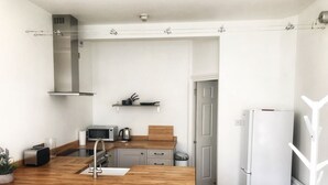Una cocina moderna con una isla de madera, taburetes blancos de bar, un microondas, un hervidor y un refrigerador blanco.