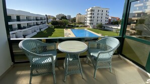 Un balcone con sedie in vimini e un tavolino, con vista su una piscina e un cortile con edifici sullo sfondo.