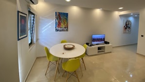 Un soggiorno moderno con un tavolo da pranzo rotondo, sedie gialle, un televisore a schermo piatto e opere d'arte alle pareti.