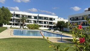 Area piscina con un edificio moderno sullo sfondo, immersa nel verde e sotto un cielo sereno.