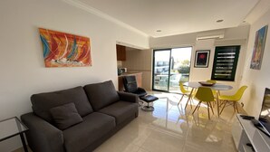 Un soggiorno moderno con un divano grigio scuro, un tavolino in vetro e un'area pranzo con sedie gialle. Una grande finestra offre luce naturale e vista sull'esterno.