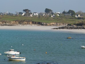 A coastal scene with boats, a sandy beach, and houses in the background.