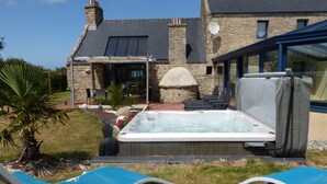 A hot tub with lounge chairs in a backyard with a stone house and a large window. - CHARACTER HOUSE: 28° covered SWIMMING POOL, SPA, JACCUZZI  (Plourin)