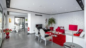 A modern living room with a dining area, a TV, and a red accent wall.