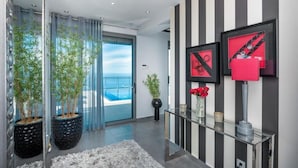 A modern interior with a glass door leading to a balcony, potted plants, a striped wall, and framed artwork.