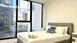 Ein modernes Hotelzimmer mit großem Fenster, einem Bett mit weißen Leinentextilien und einem grauen Kopfteil.