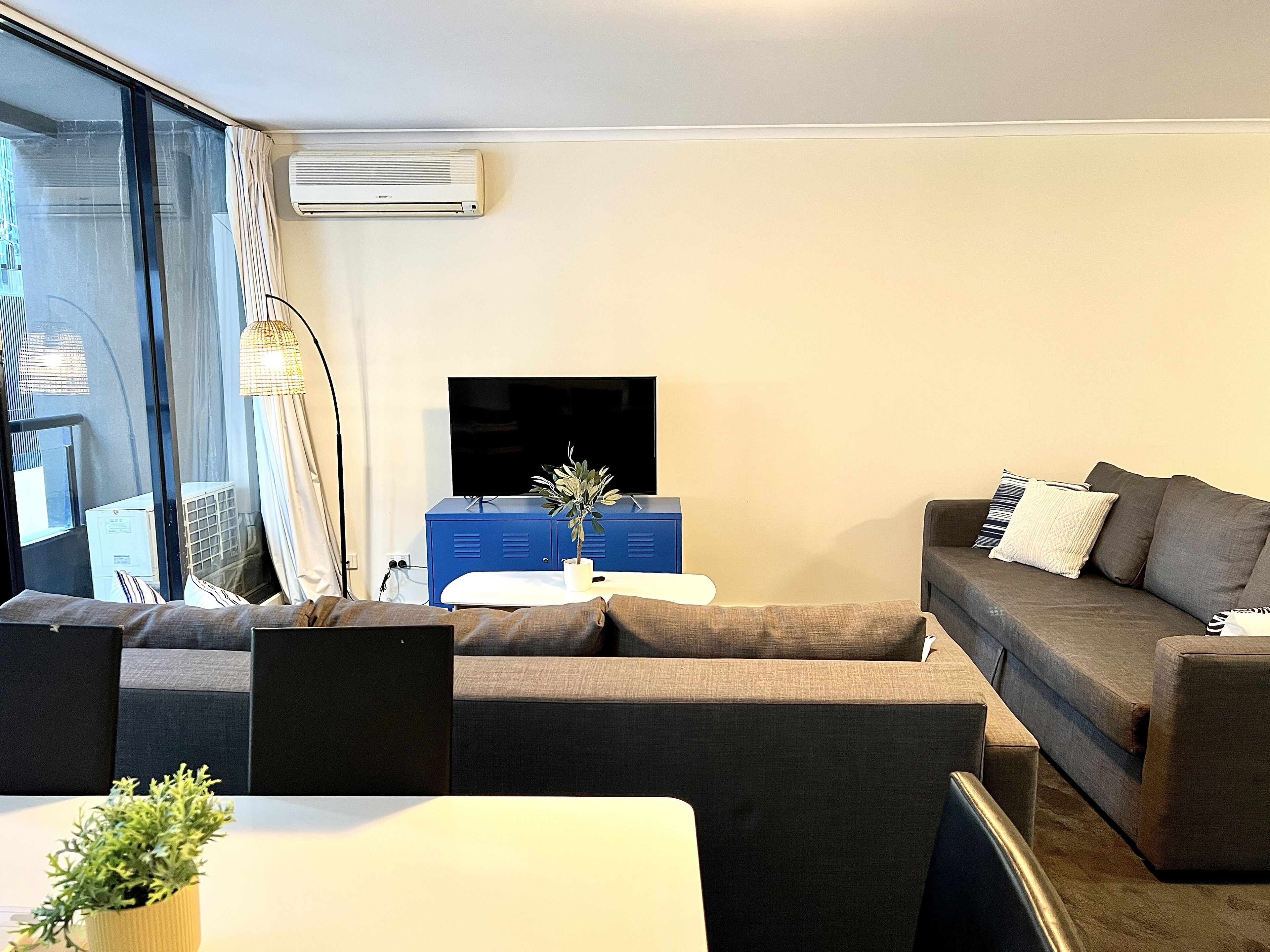 Ein modernes Wohnzimmer mit einer Couch, einem kleinen Tisch, einem Fernseher und einer Topfpflanze.