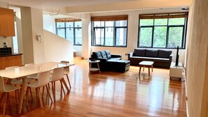 Un salón espacioso con suelo de madera, una mesa de comedor con sillas, un sofá y una pequeña mesita auxiliar.