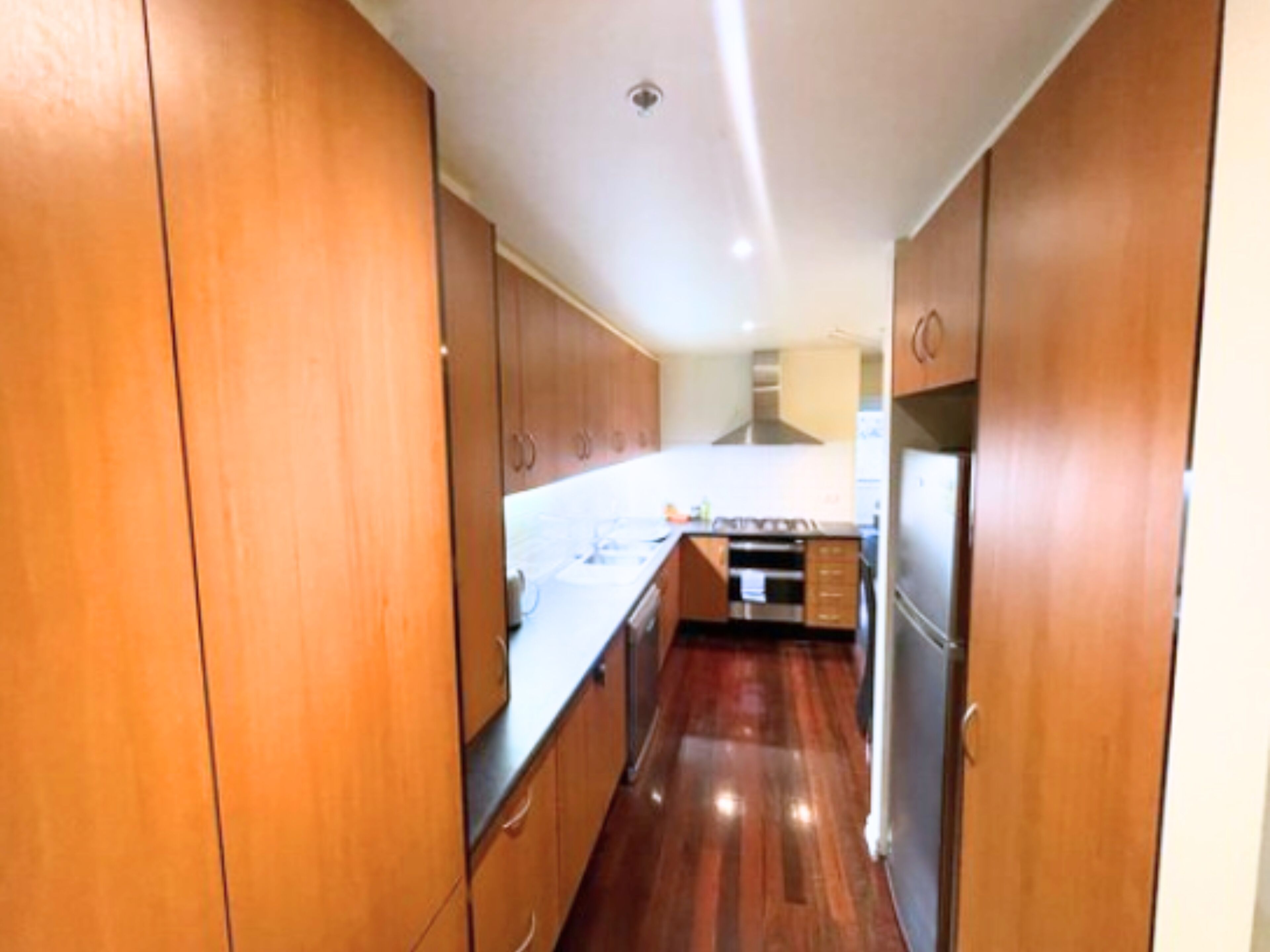 A narrow kitchen with wooden cabinets and a stainless steel range hood.