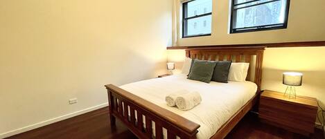 A bedroom with a wooden bed, two bedside lamps, and two windows.
