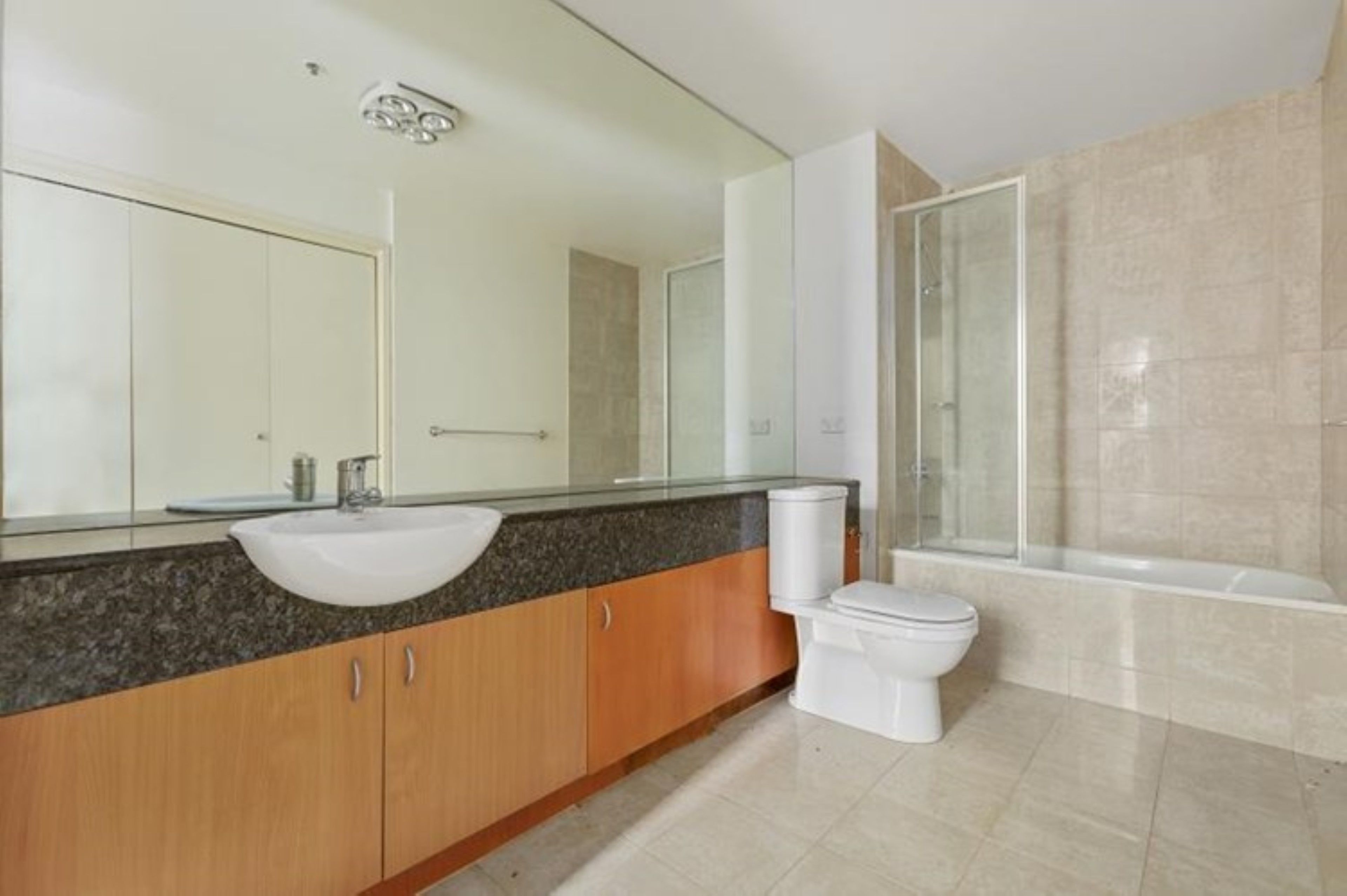 Un baño moderno con encimera de granito, lavamanos blanco, inodoro y ducha con mampara de vidrio.