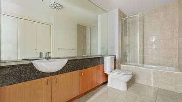 Un baño moderno con encimera de granito, lavamanos blanco, inodoro y ducha con mampara de vidrio.