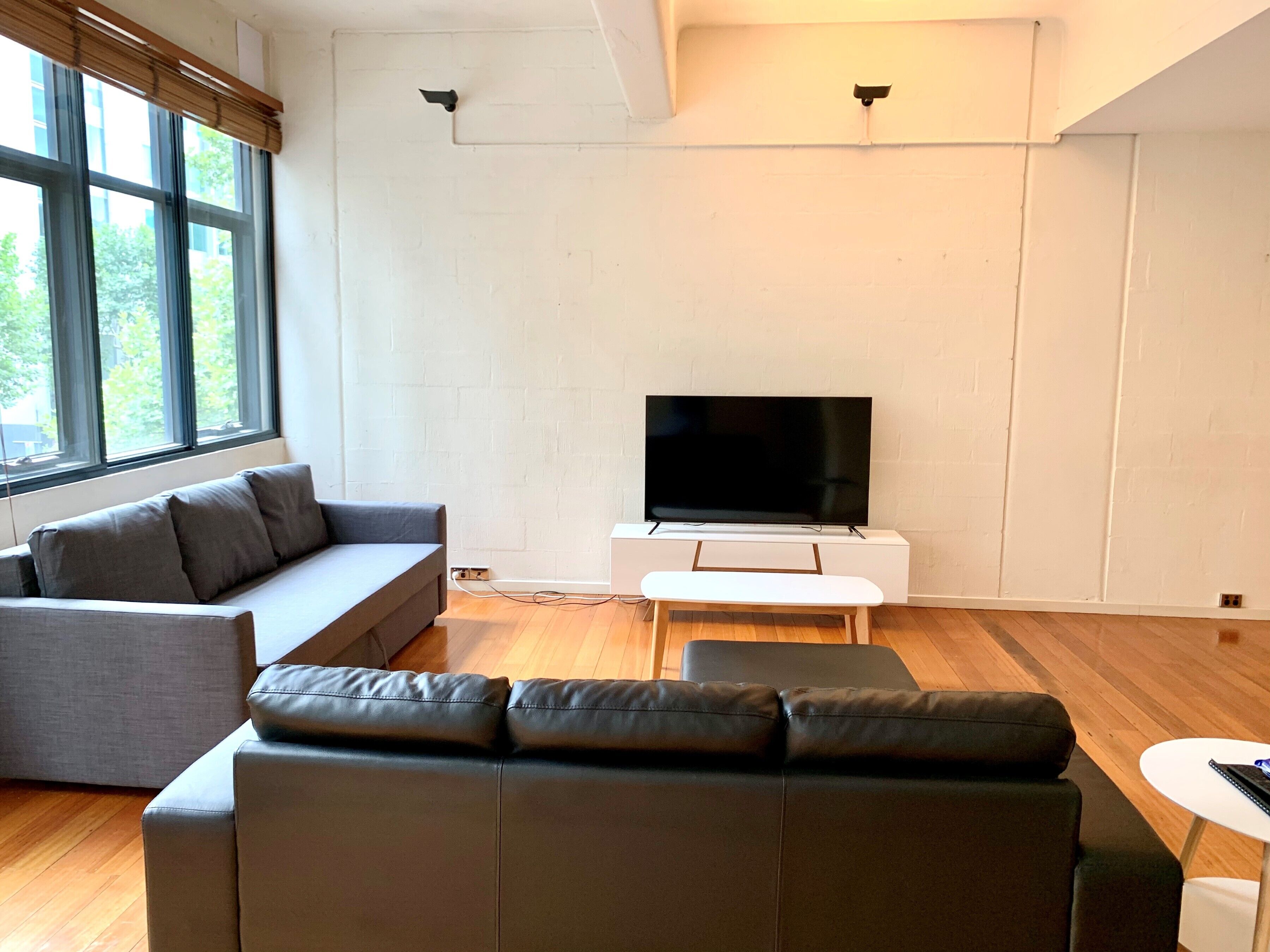 A modern living room with a grey sofa, a black leather couch, a white coffee table, and a flat-screen TV on a white stand.