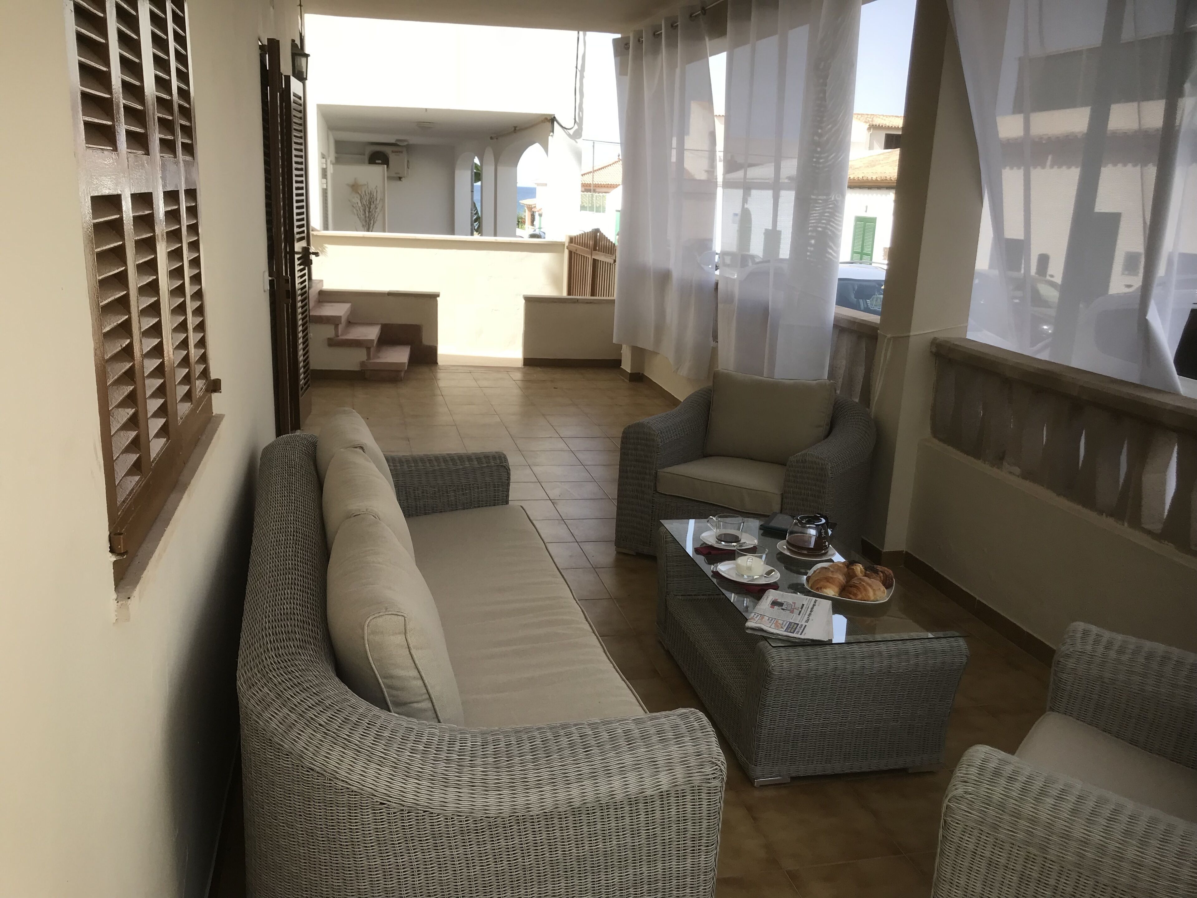 A balcony with wicker furniture, a coffee table with breakfast items, and a view of a building in the background.