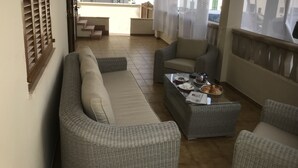A balcony with wicker furniture, a coffee table with breakfast items, and a view of a building in the background.