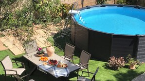 A backyard with a swimming pool, a dining table with chairs, and various plants.